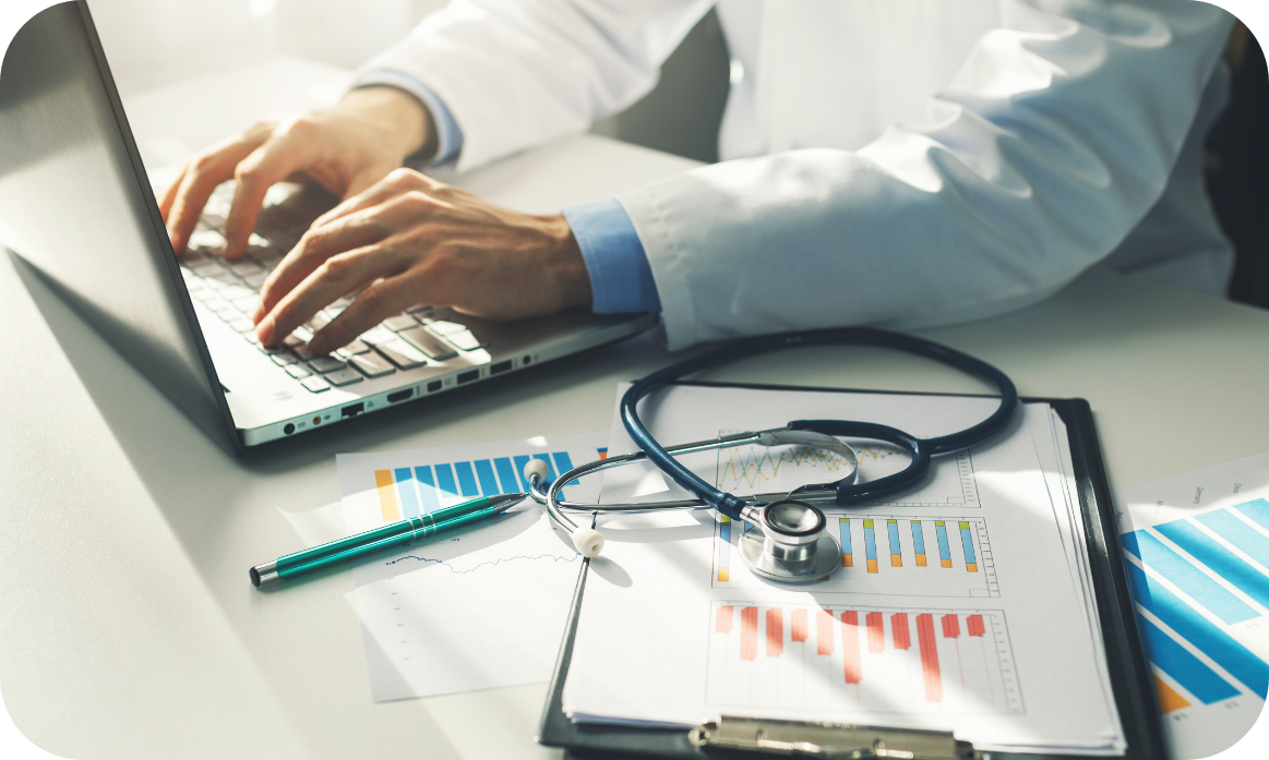 Healthcare professional reviewing data on a laptop beside a stethoscope